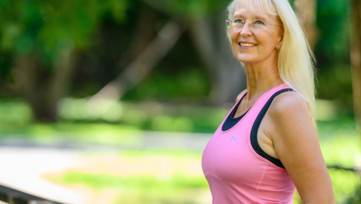 Woman in pink athletic tank top smiling outdoors with blurred green background.