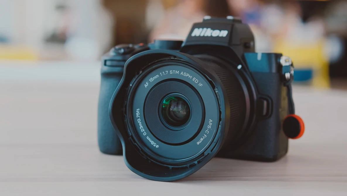 Nikon mirrorless camera with blue body and standard zoom lens on neutral surface.