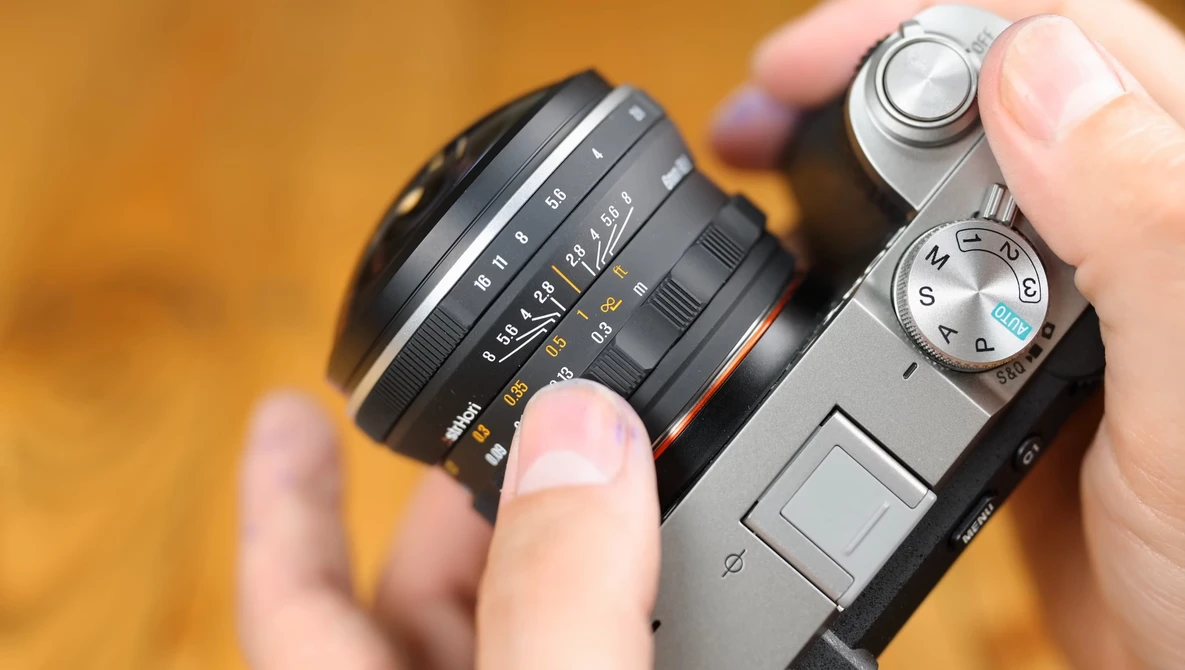 Hands holding a vintage rangefinder camera with an interchangeable lens mounted on top.