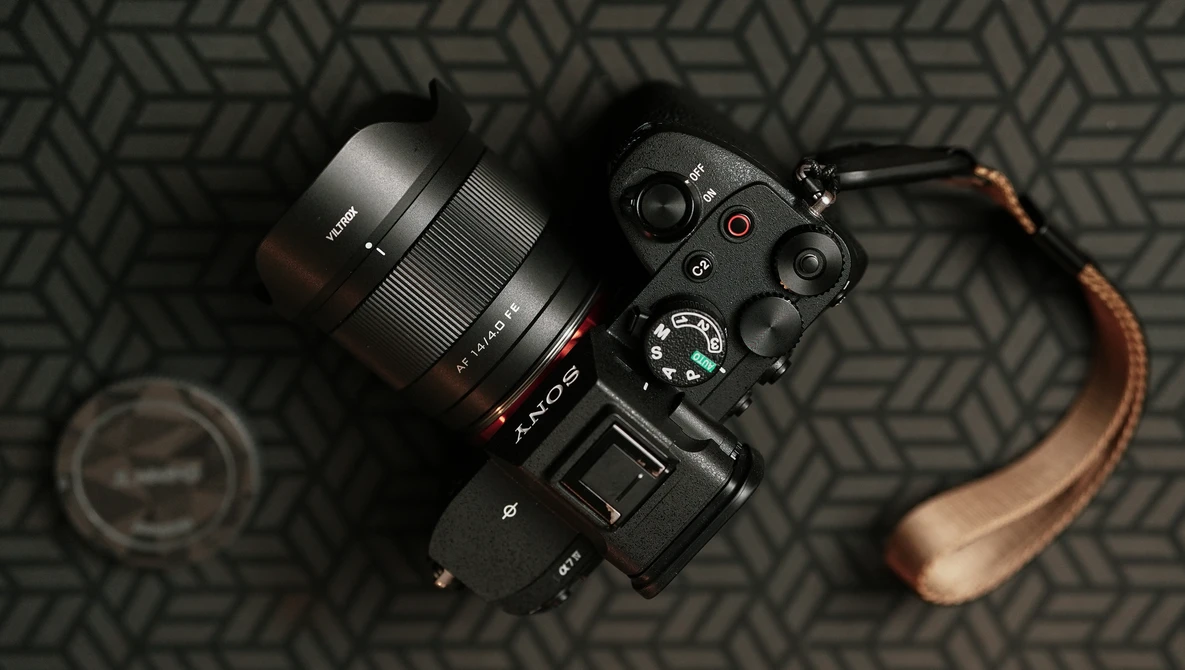 Sony mirrorless camera with attached lens and brown leather strap on geometric patterned surface.