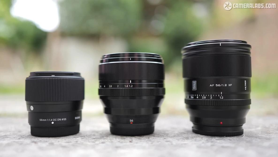 Three black camera lenses arranged in size progression on concrete surface outdoors.