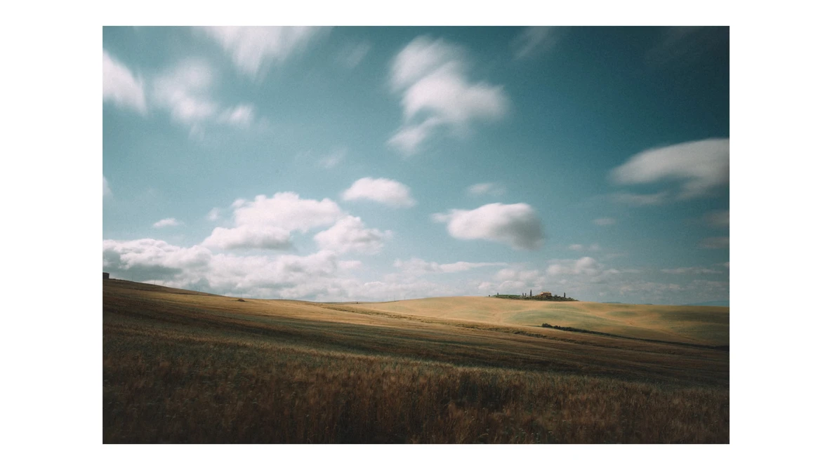 Rolling agricultural landscape with plowed and golden fields under a partly cloudy sky.