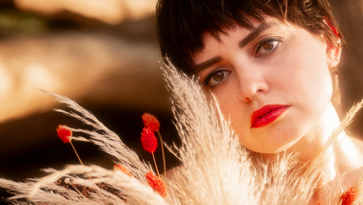 Portrait of a woman with dramatic red lipstick framed by wheat stalks and red berries.