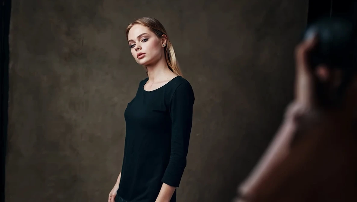 Woman in black long-sleeve shirt posed against textured neutral background.