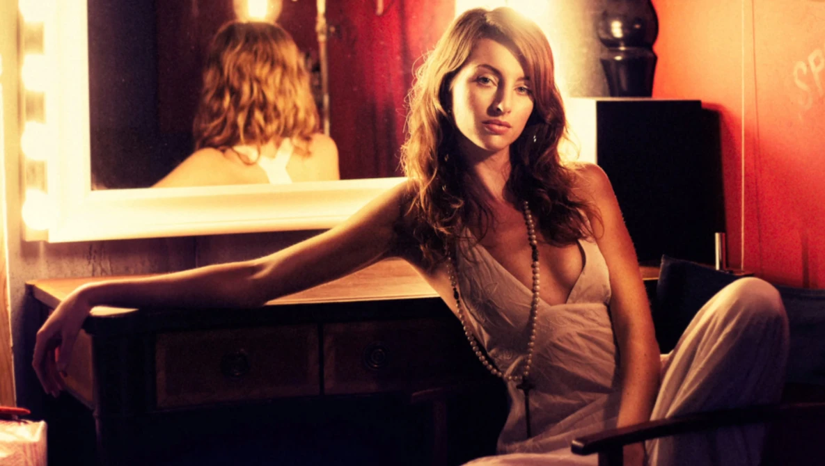 Woman at vanity mirror with warm golden lighting and red backdrop.
