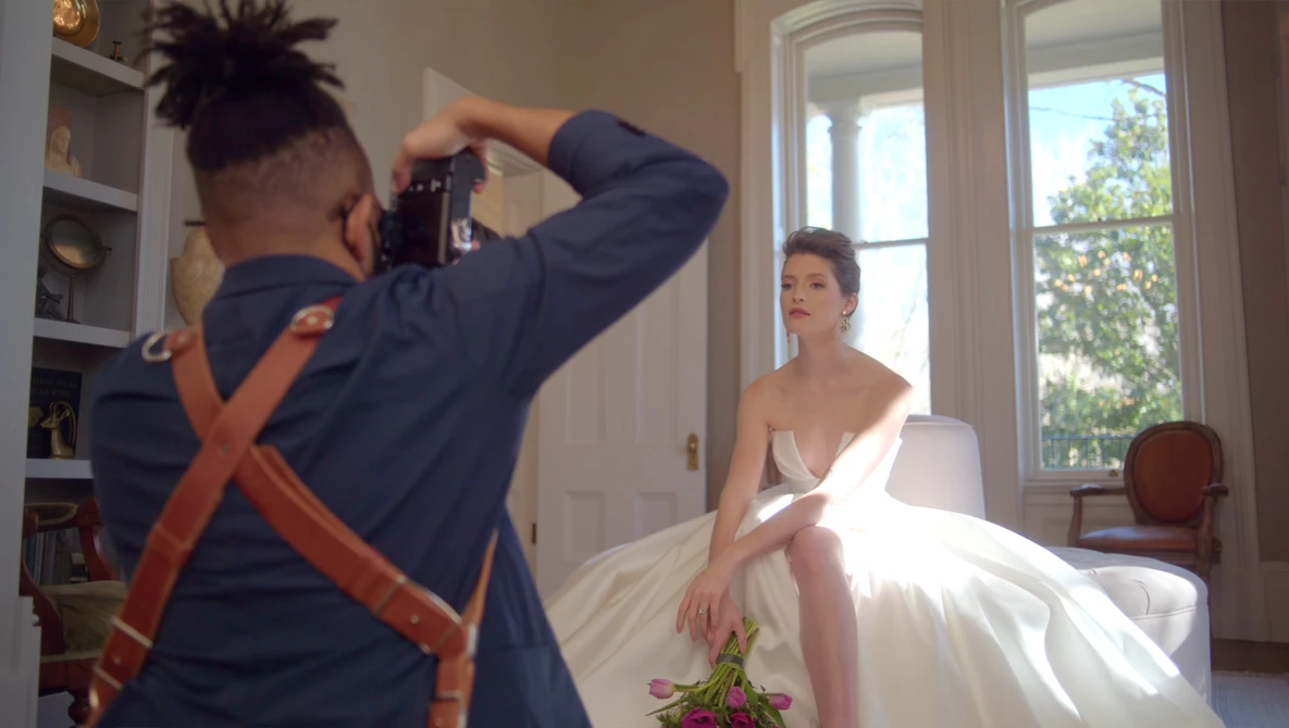 Photographer capturing a portrait of a woman in a white wedding dress during an indoor photo shoot.