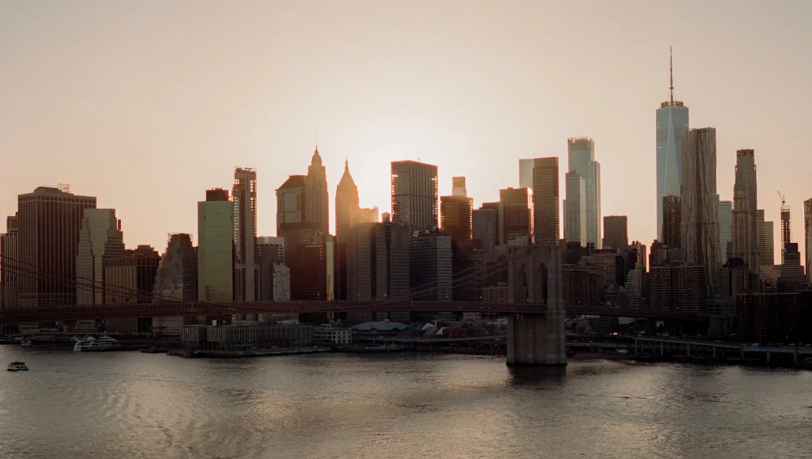 Manhattan skyline at golden hour with waterfront and bridge in foreground.