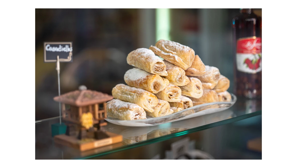 Stacked pastry rolls dusted with powdered sugar displayed on a white plate behind a glass bakery counter.