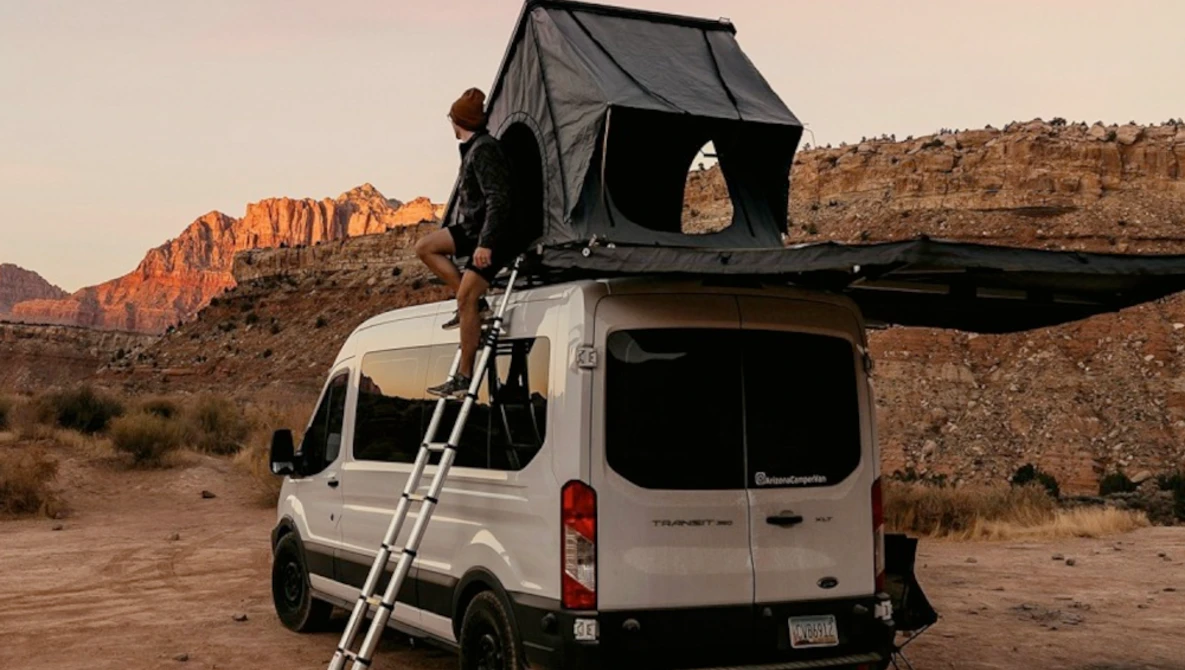 White van with open roof tent in desert landscape during golden hour.