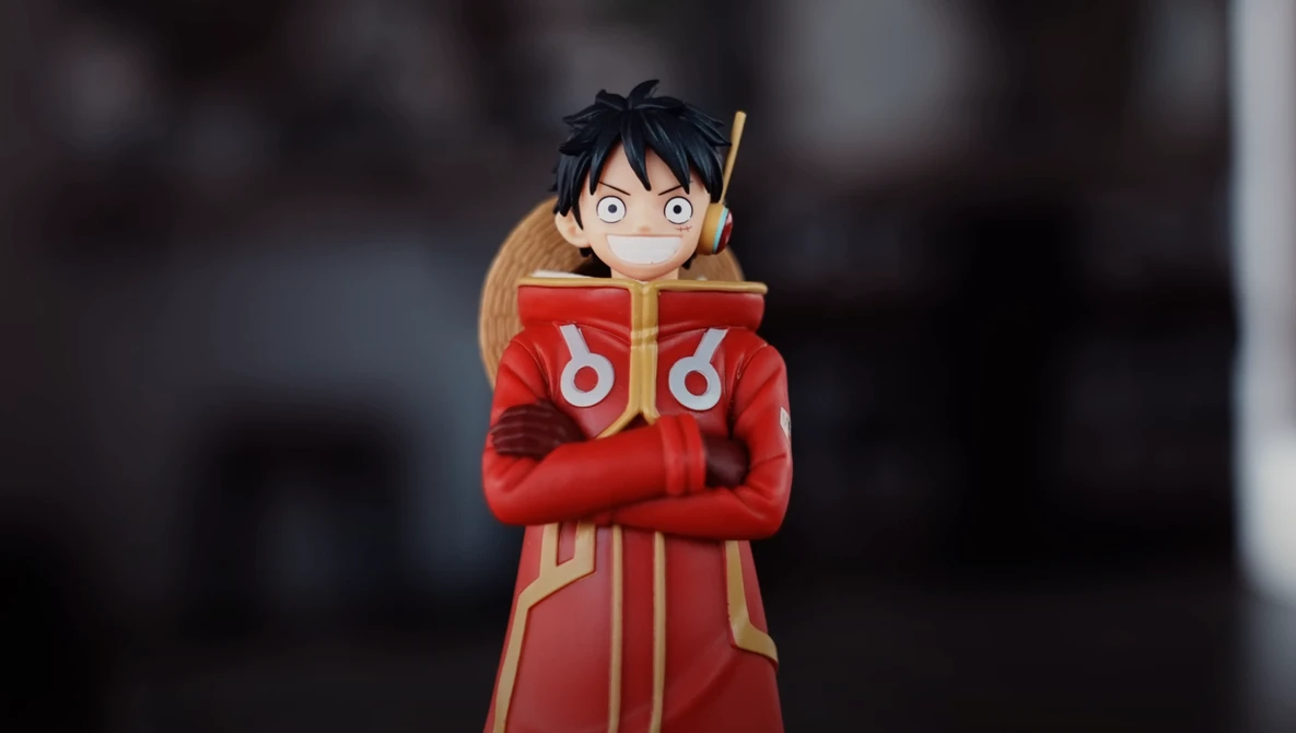 Illustration of an anime character with black hair wearing a red and gold coat with crossed arms.