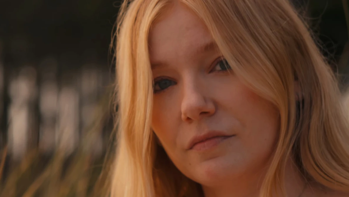 Woman with long reddish-blonde hair gazing downward with a contemplative expression.