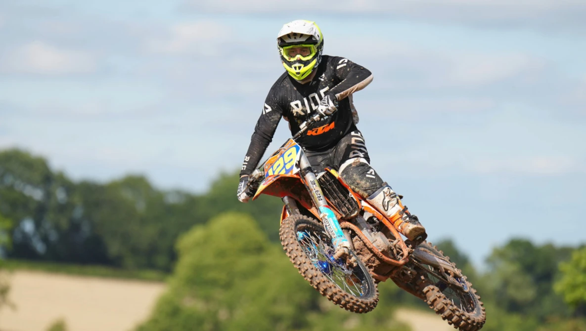 Motocross rider airborne on dirt bike mid-jump against cloudy sky.