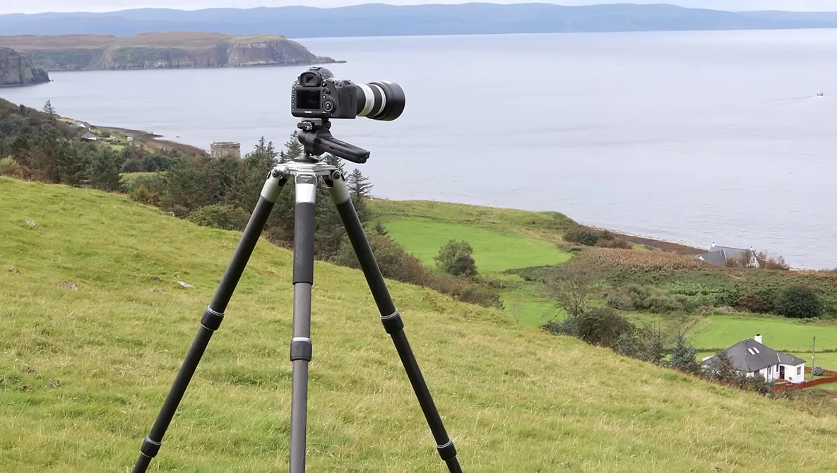 Camera mounted on tripod overlooking coastal landscape with mountains and water.
