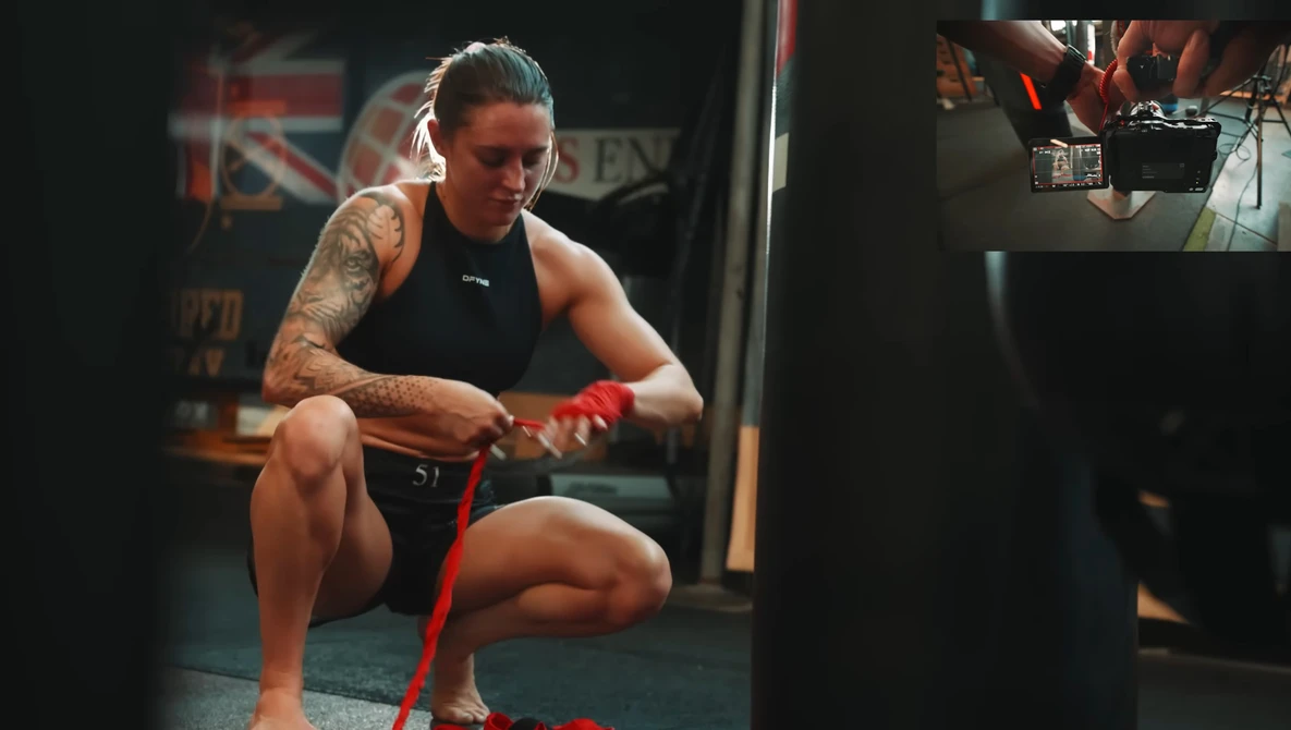 Athlete in black tank top performing a squat with a red resistance band in a gym.