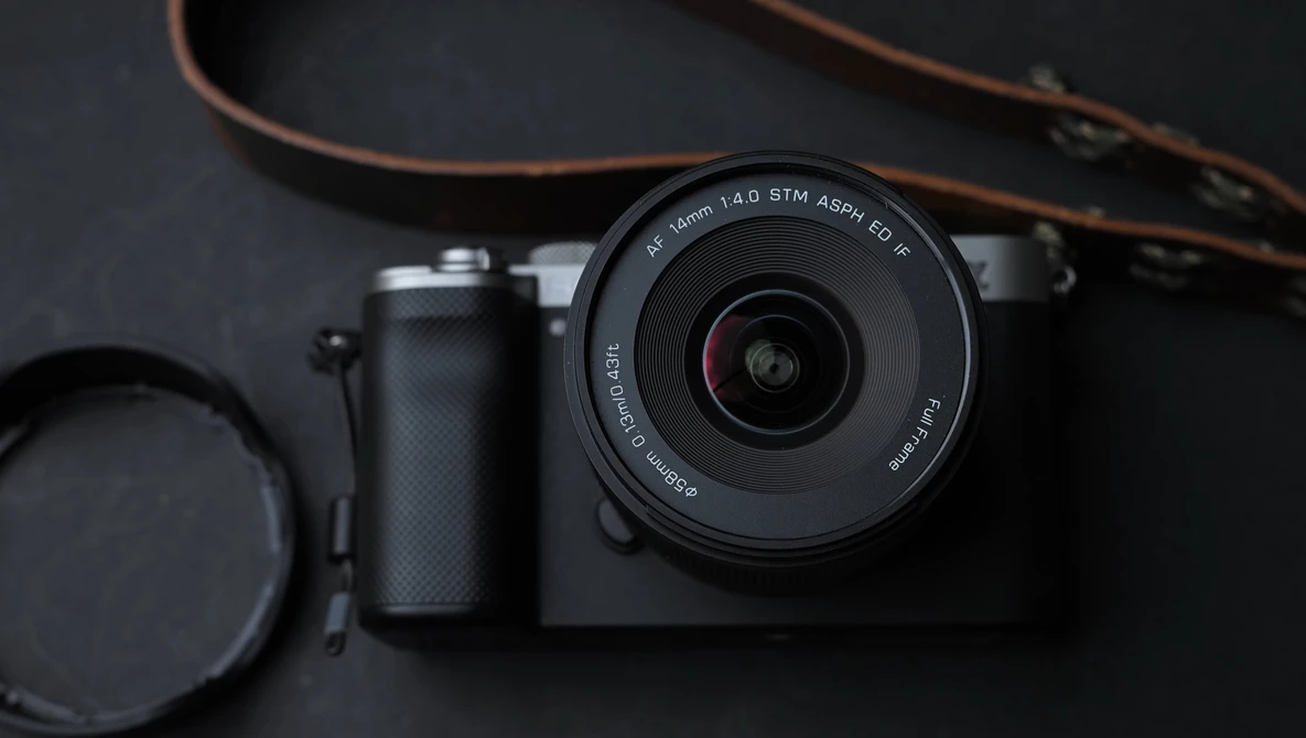 Mirrorless camera with prime lens, lens cap, and brown leather strap on dark surface.