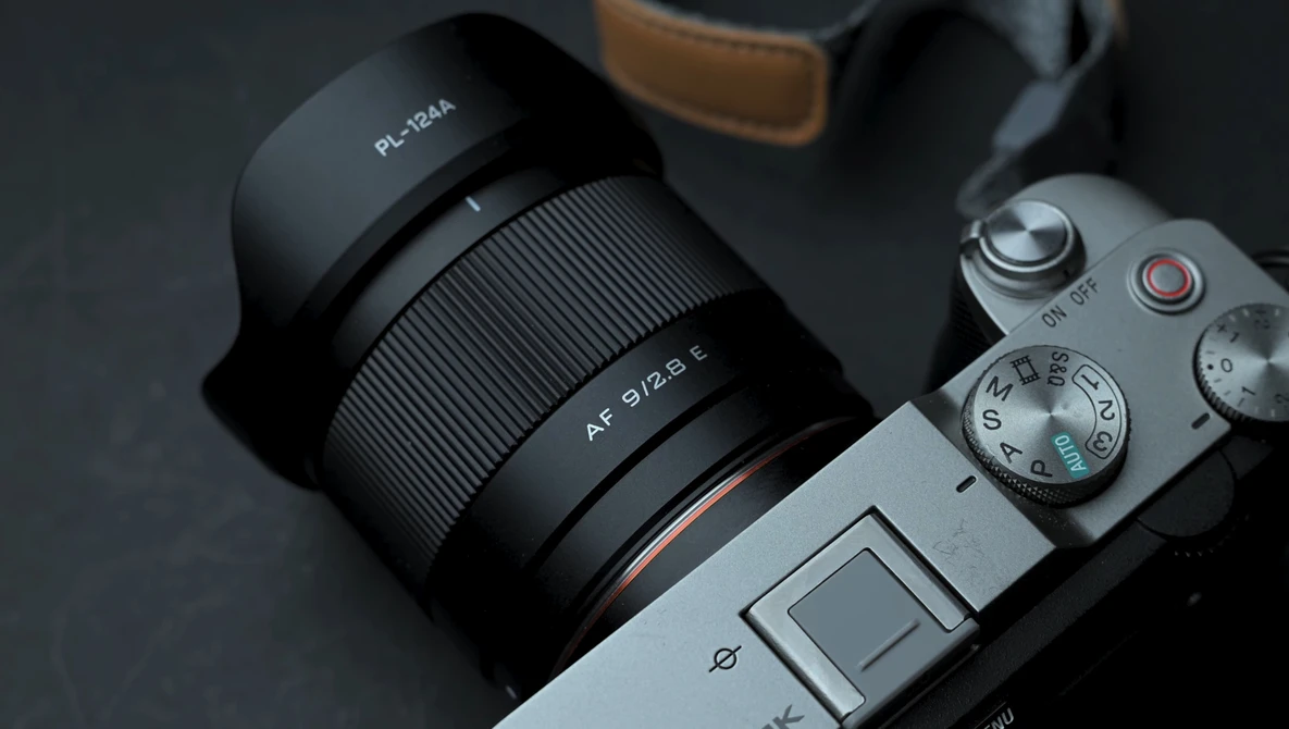 Mirrorless camera with wide-angle lens mounted, showing manual focus ring and aperture markings.