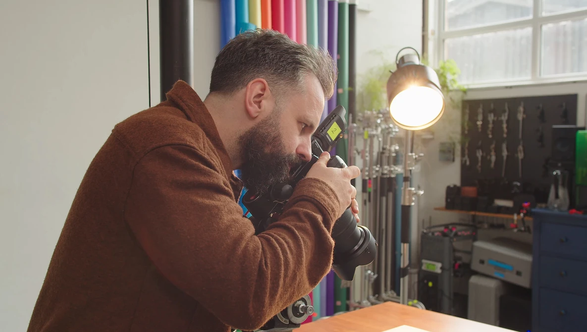 Photographer looking through camera viewfinder in studio with professional lighting setup.