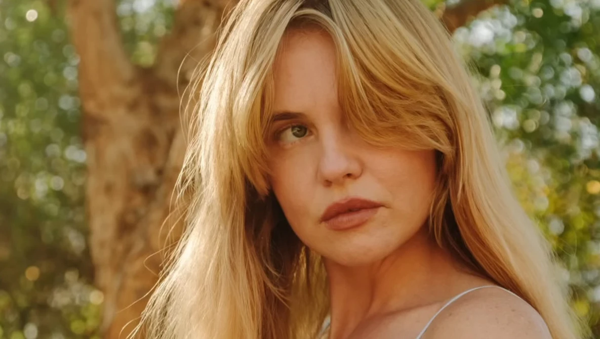 Young woman with long blonde hair gazing over shoulder in natural outdoor setting.