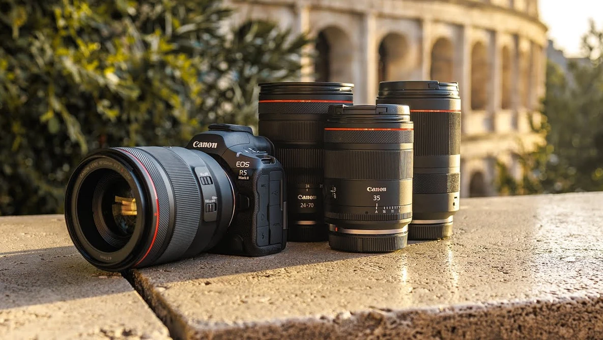Canon EOS R5 camera with RF mount lens surrounded by three additional Canon RF lenses on stone surface.