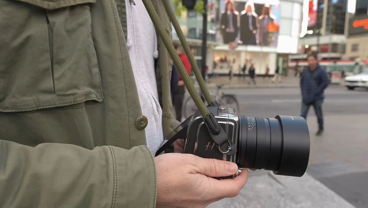 Photographer holding a mirrorless camera with telephoto lens on a city street.