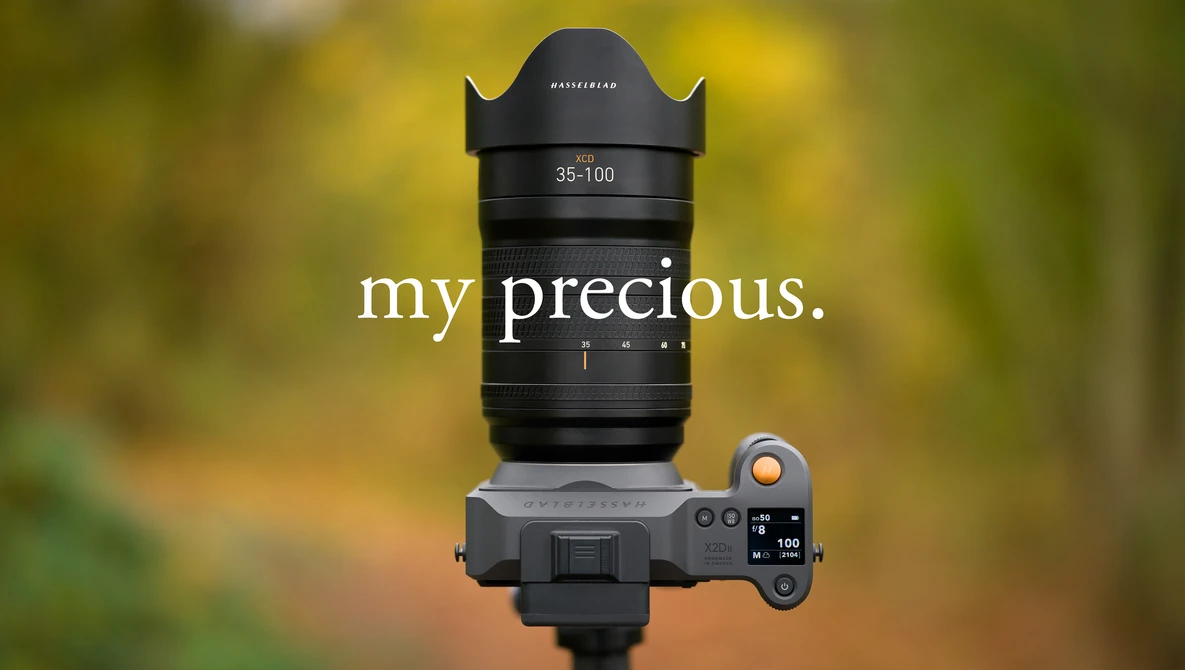 Hasselblad 35-100mm zoom lens mounted on a mirrorless camera body against a blurred green and yellow background.