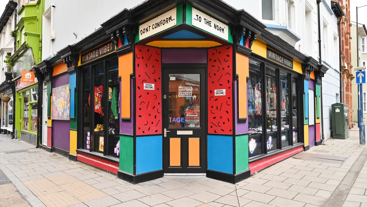 Vibrant corner storefront with bold primary colors, geometric patterns, and black framing on a brick street.