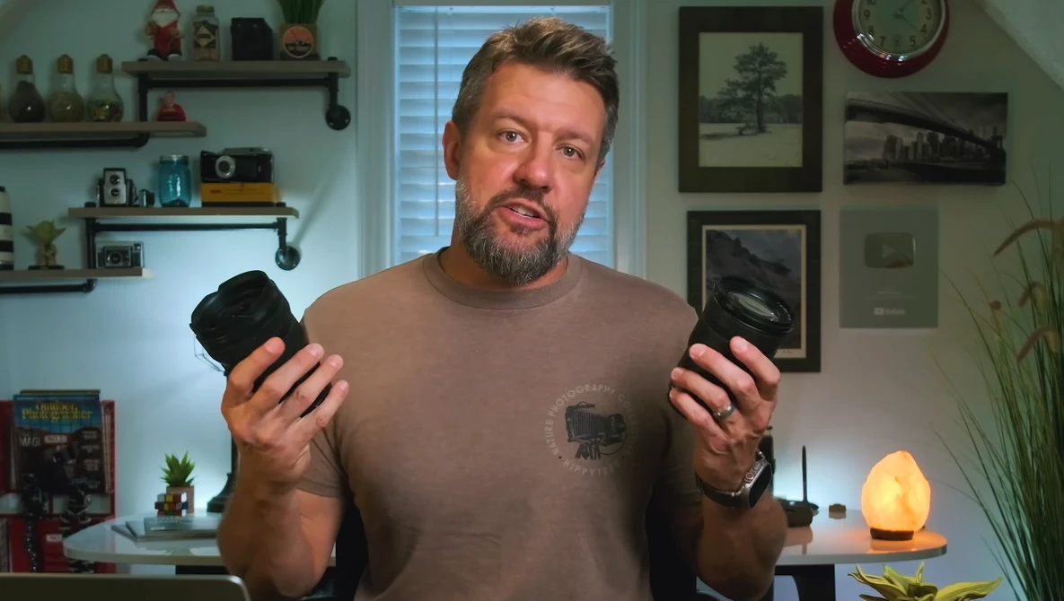 Man holding two camera bodies while discussing photography equipment in a home studio setting.