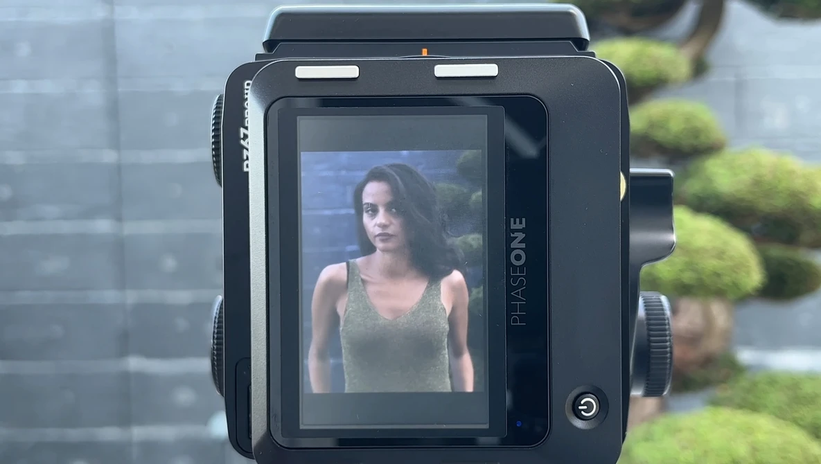 Medium format camera displaying a portrait of a woman on its rear LCD screen in outdoor daylight.