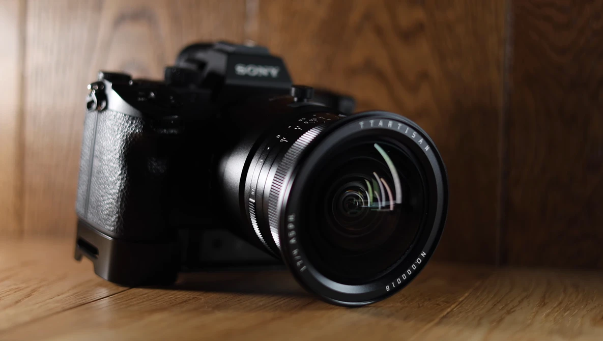 Sony mirrorless camera with wide-angle lens on wooden surface under warm studio lighting.