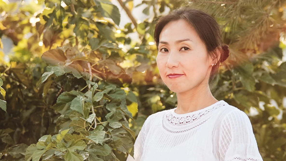 Woman in light-colored lace top poses among foliage during golden hour.