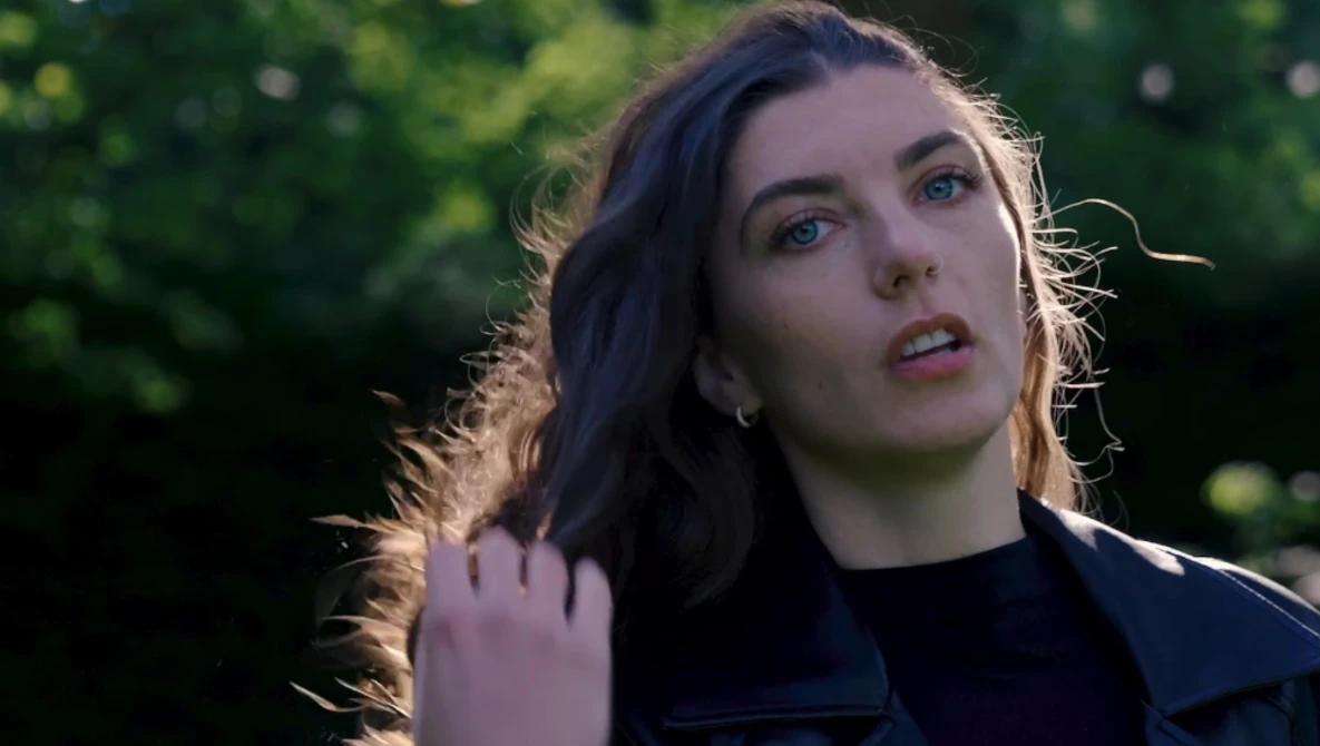 Woman with dark hair looking upward in golden hour sunlight against blurred green foliage.