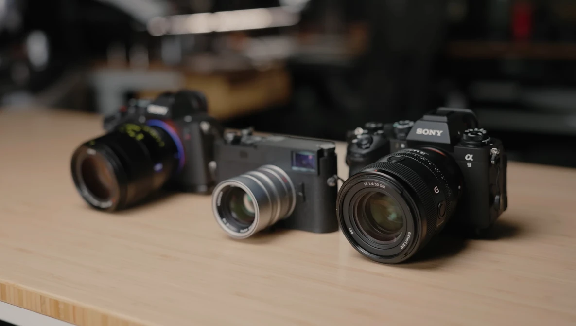 Three mirrorless cameras arranged on a wooden table, displaying different lens and body configurations.
