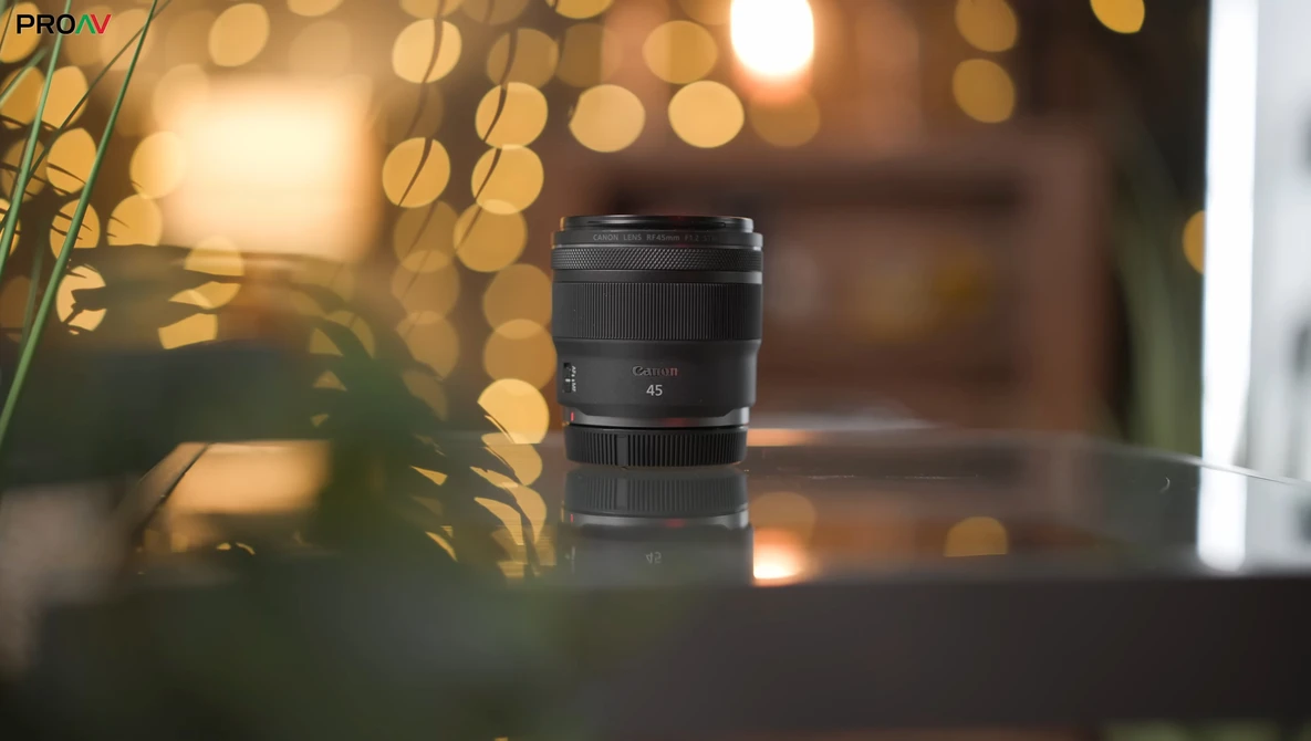Black camera lens displayed on a surface with warm bokeh lights and foliage in the background.