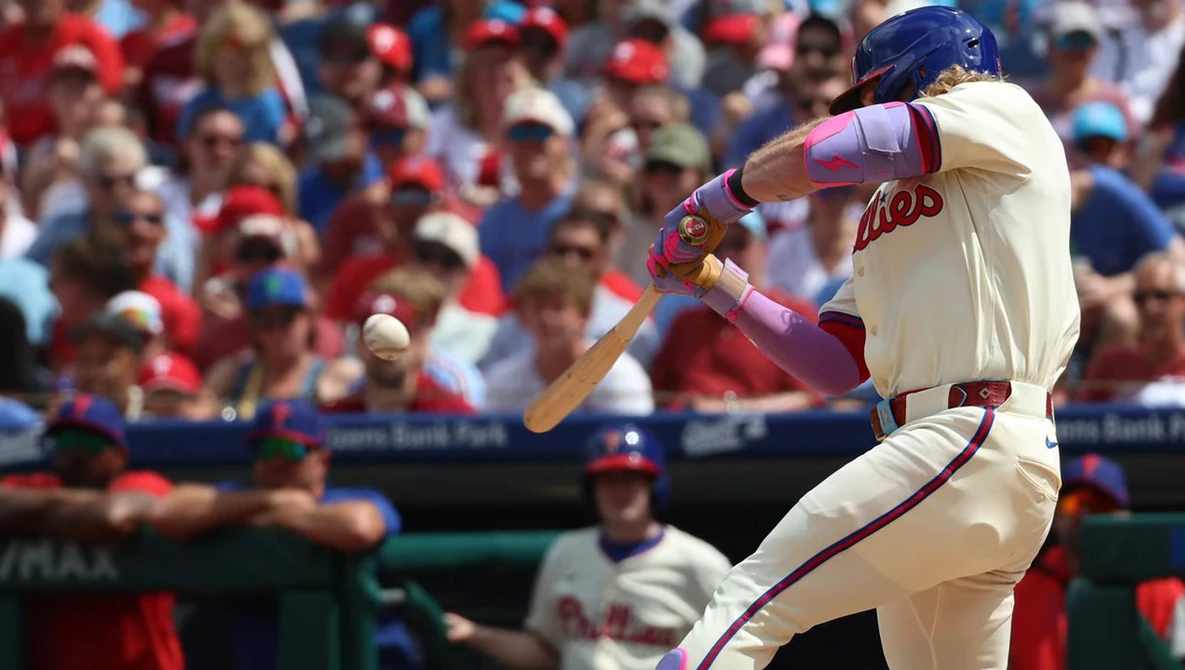 Baseball player mid-swing at the plate during a day game with crowded stadium in background.