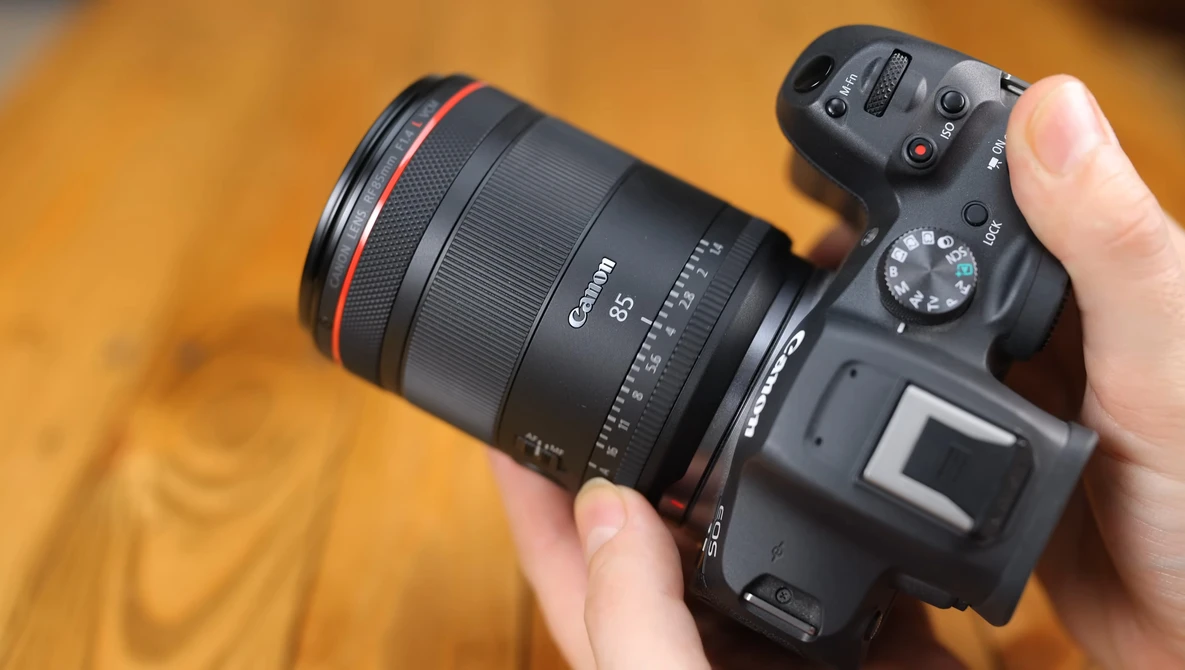 Canon mirrorless camera with RF-mount lens held in hand against warm wooden background.
