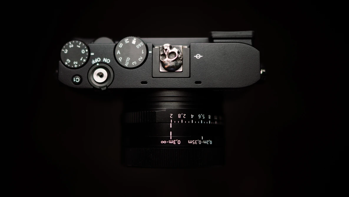 Top-down view of a rangefinder camera with dark gray body, showing dials, shutter button, and attached black lens.