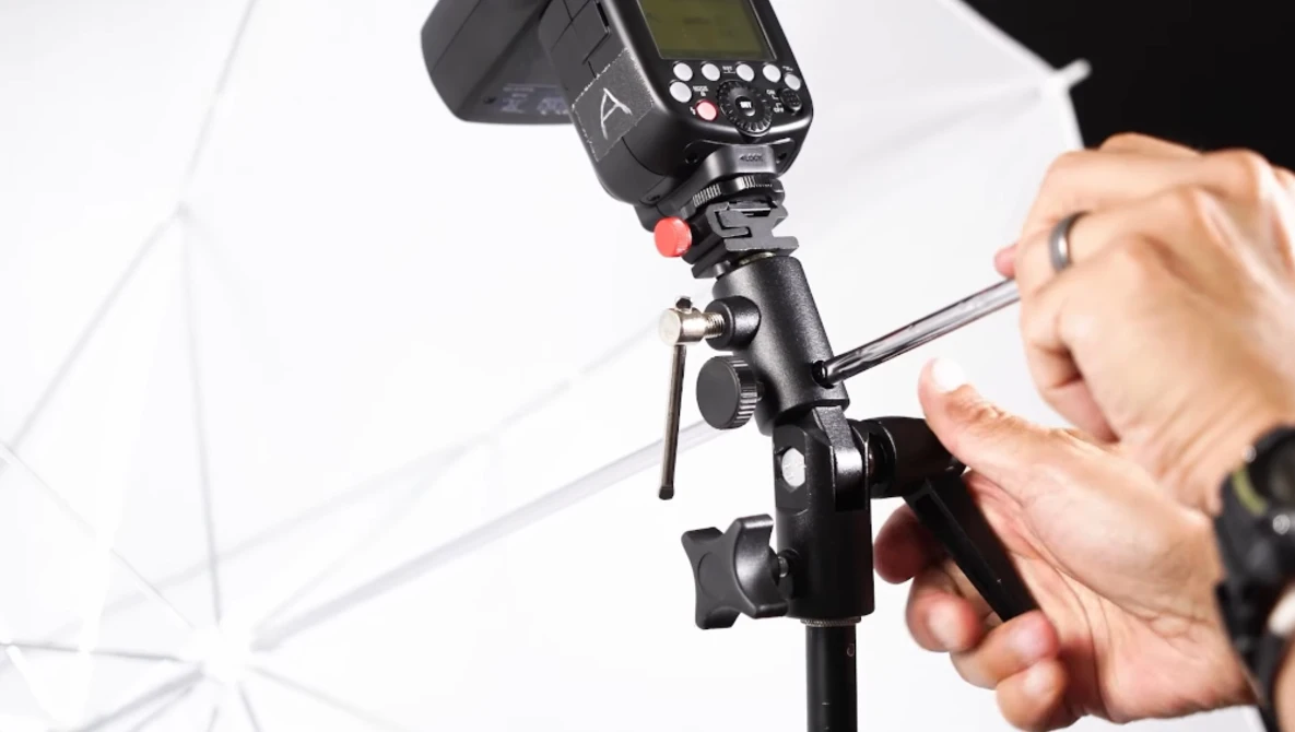Photographer adjusting a flash unit mounted on a light stand with white umbrella diffuser.