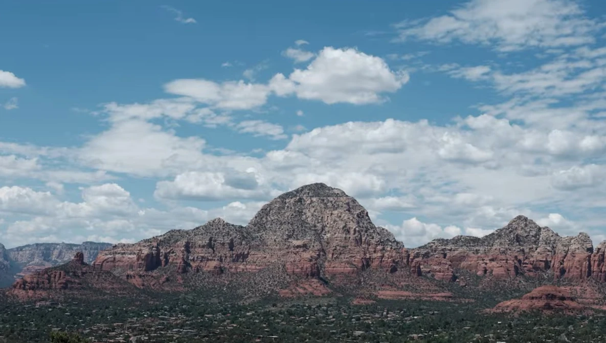 Desert mountain range with red rock formations beneath a partly cloudy blue sky.
