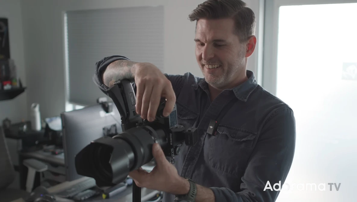 Photographer holding a professional cinema camera with a large lens attachment in a bright studio setting.