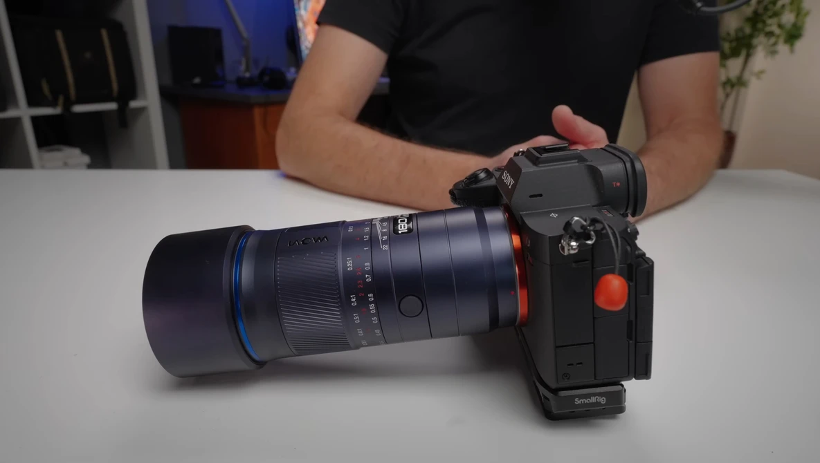 Camera with telephoto lens attached, displayed on white table with person in black shirt behind it.
