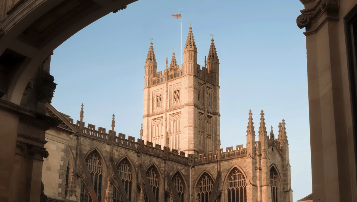 Gothic cathedral tower framed by classical stone archway, photographed during golden hour.