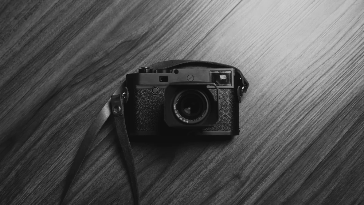 Rangefinder camera with attached strap positioned on diagonal striped wooden surface.