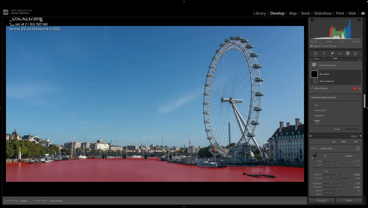 London Eye ferris wheel and Thames riverbank under clear blue sky, with red-tinted water in foreground.