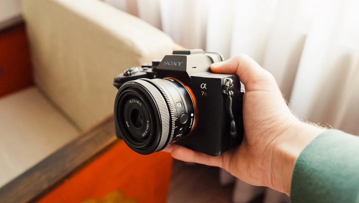 Hand holding a Sony Alpha mirrorless camera with a compact prime lens attached, indoors.
