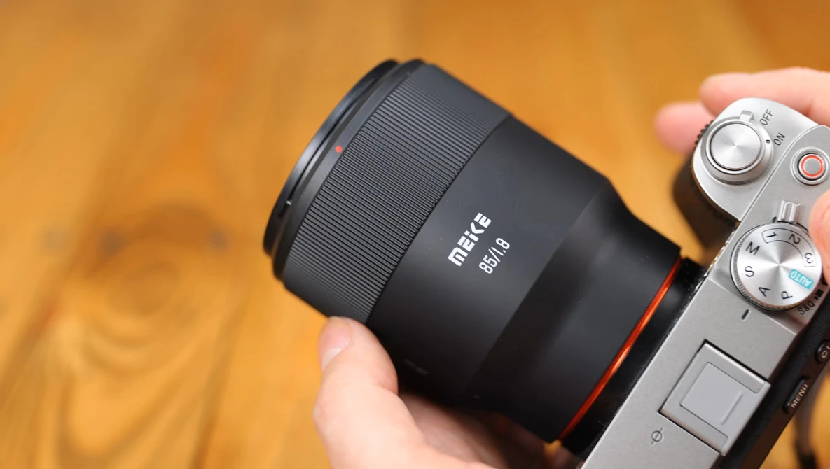 Metus 85mm lens mounted on a mirrorless camera, held in someone's hand against a warm, blurred background.