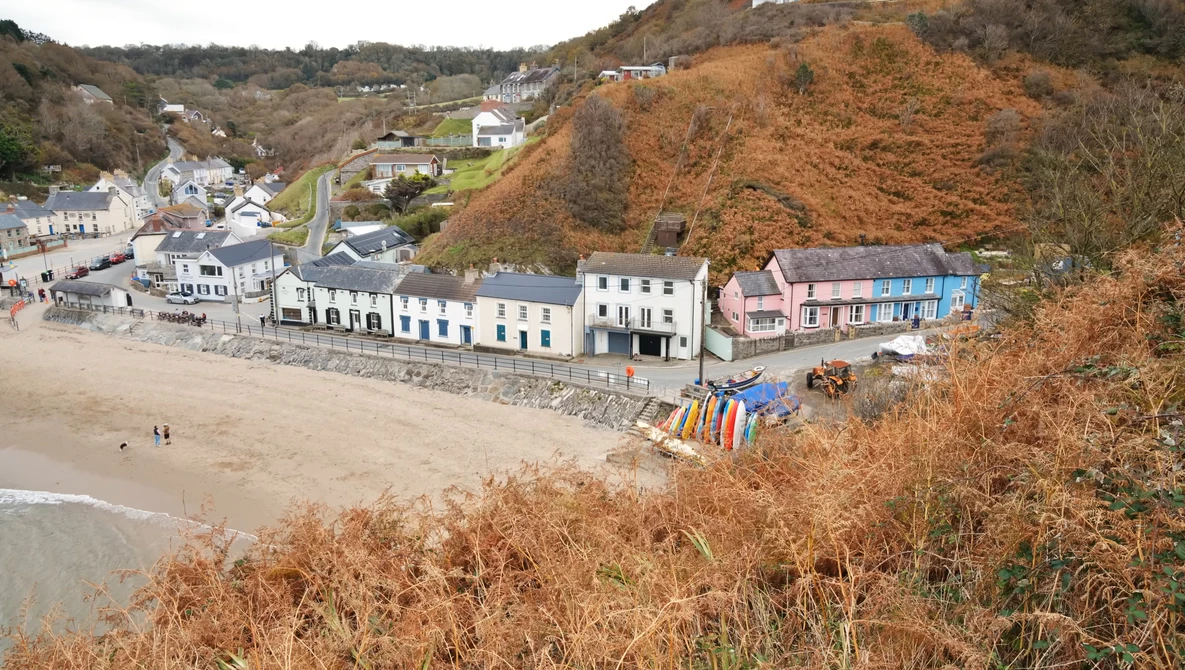 Coastal village nestled against a steep cliff with colorful beach huts and stone buildings along the shoreline.