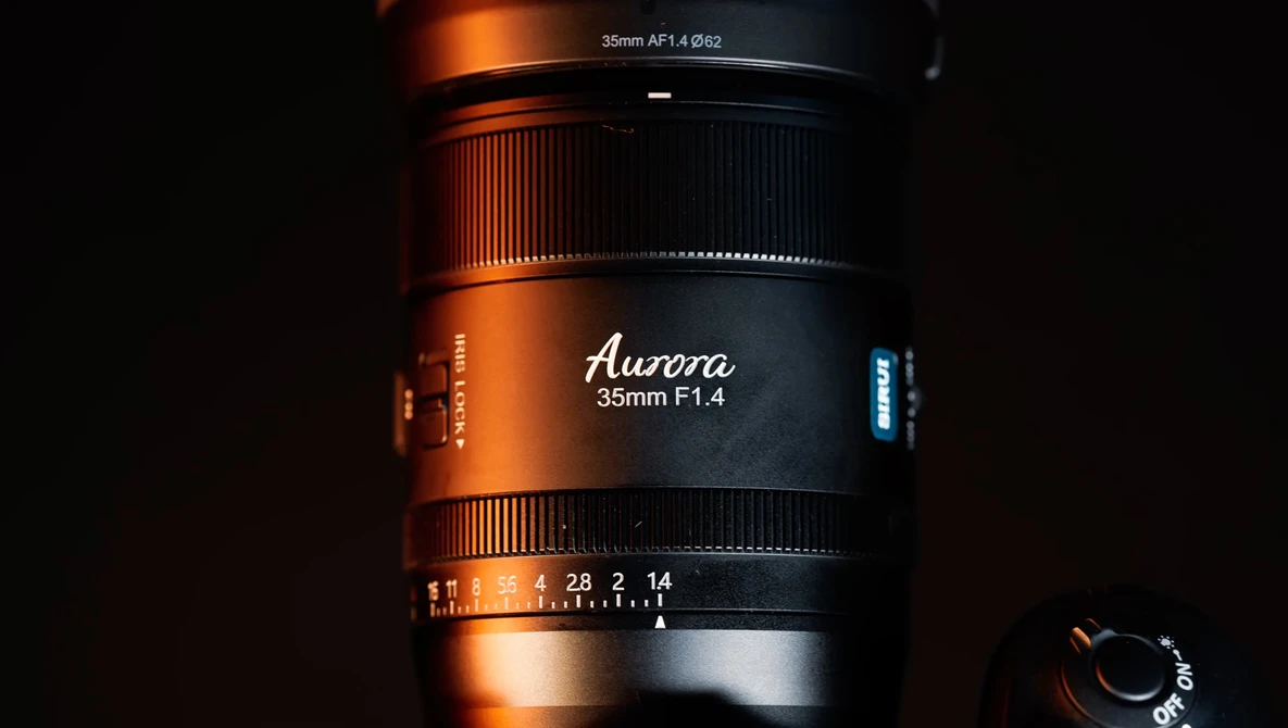 Aurora 35mm F1.4 lens with focus and aperture rings visible against dark background with dramatic orange and blue lighting.