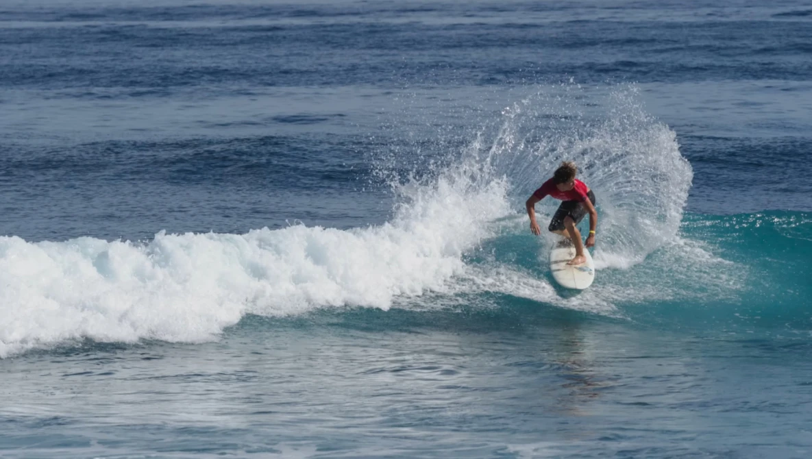 Surfer riding a turquoise wave in a red board shorts, angled into the curl of white foam.