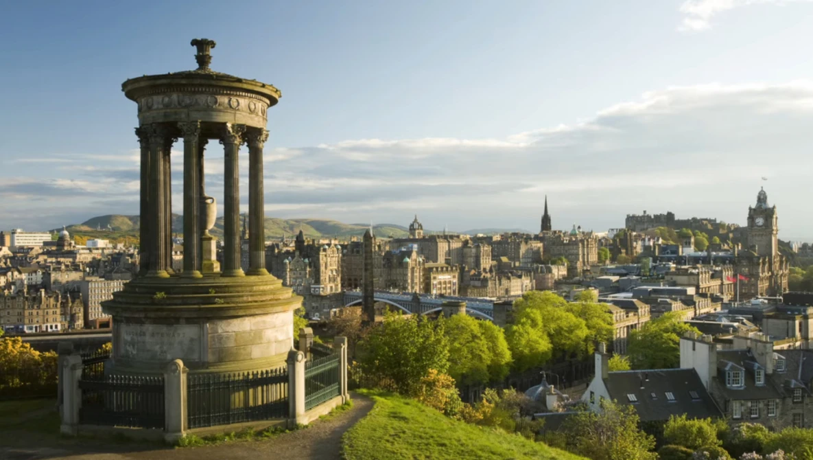 Stone monument with columned rotunda overlooking a historic cityscape with church spires and buildings.