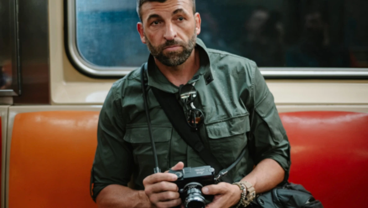 Man holding a vintage camera on public transit, wearing a green utility shirt.